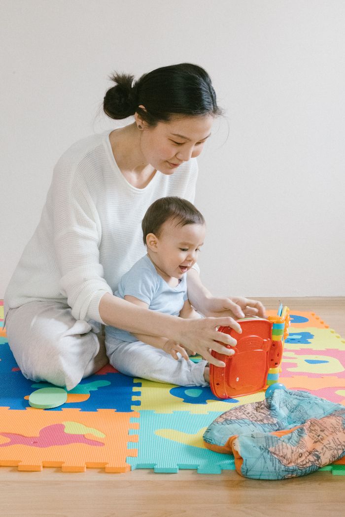 Mother and baby playing with toy on colorful puzzle mat indoors.